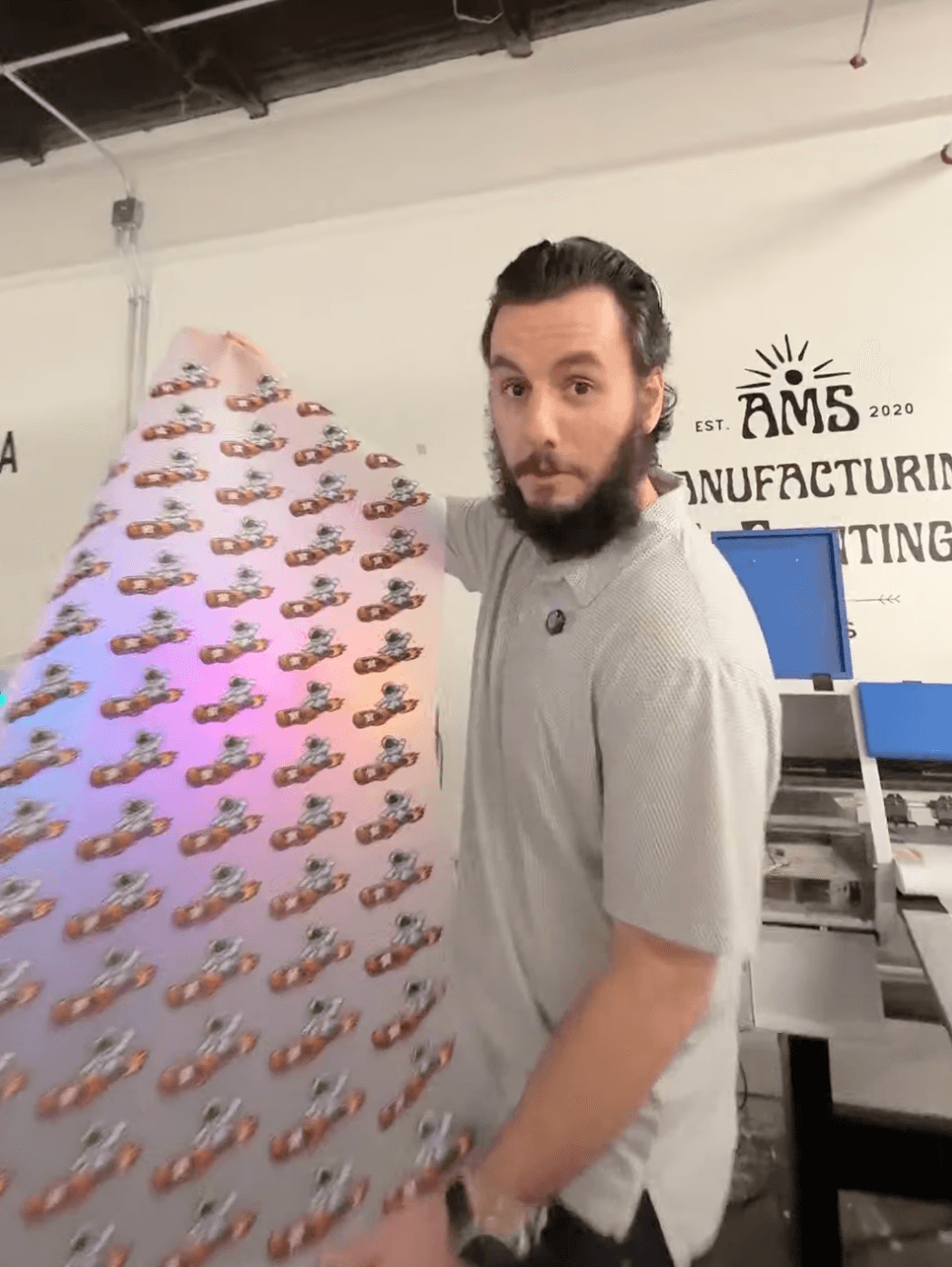 Alex from AMS holding a DTF gang sheet in front of the production printer