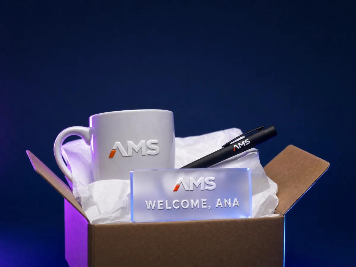 A welcome kit in an open box: a mug, a pen, and a small acrylic name plate carrying the same logo
