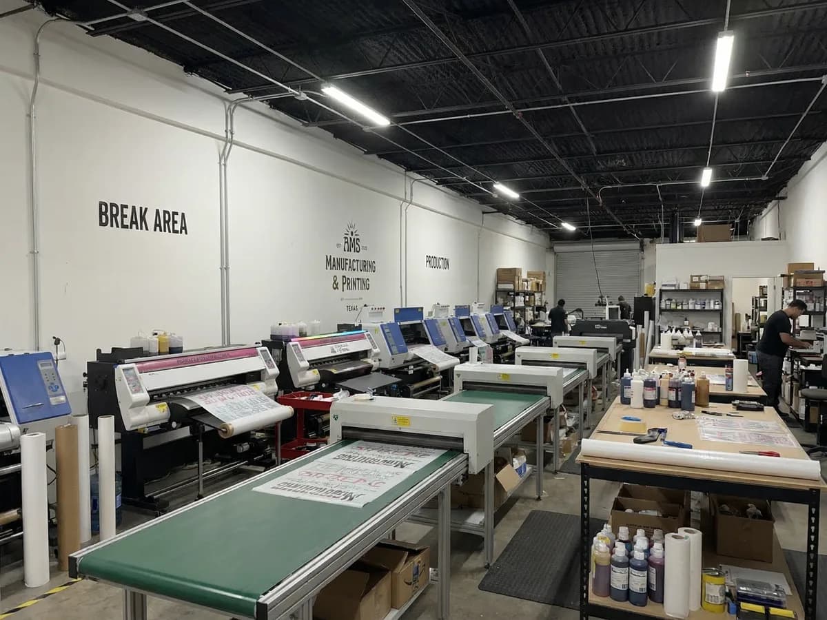 AMS Transfers production floor in Houston with DTF printers and stacks of custom printed shirts